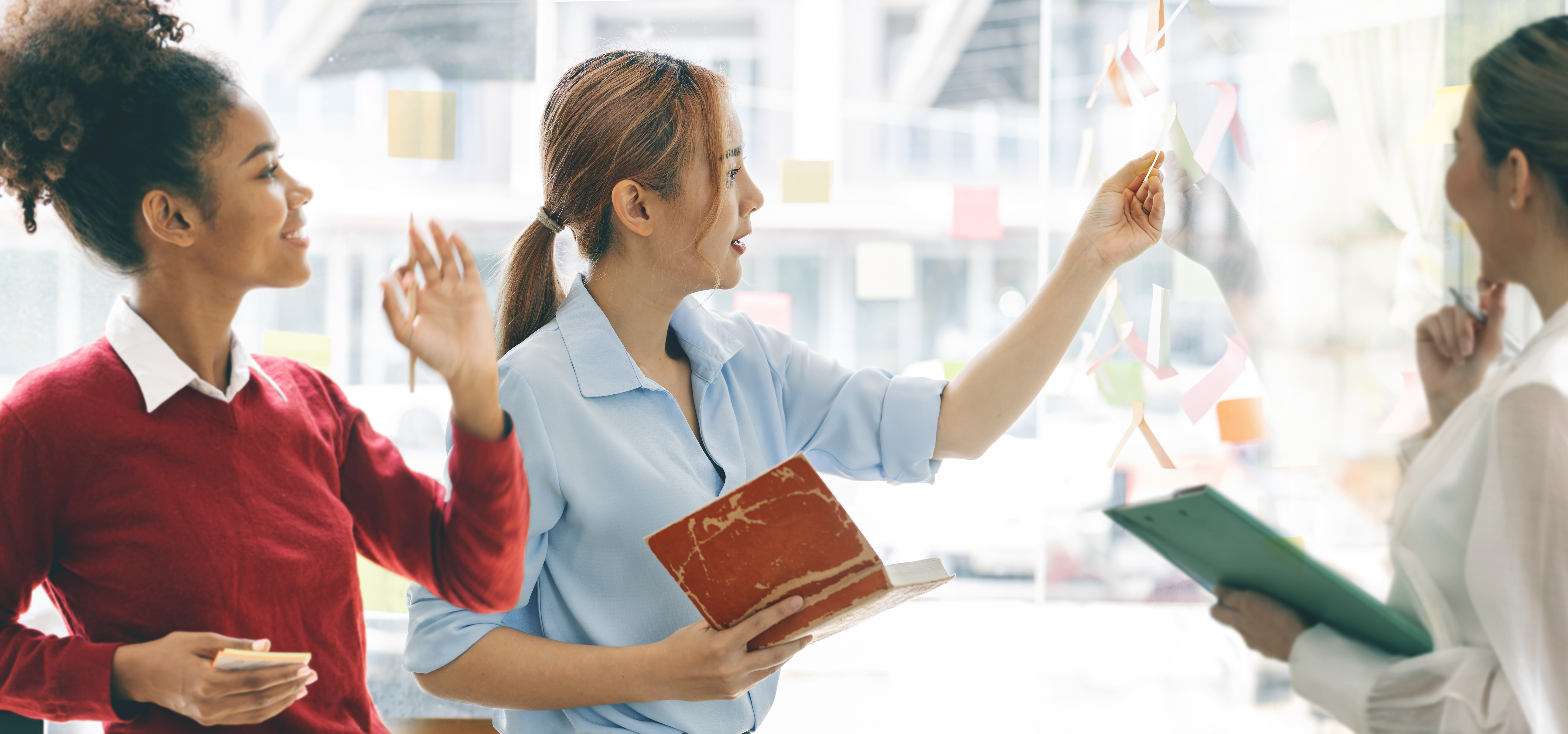 © nampix | freepik.com | Junges kreatives Geschäftsfrauenteam diskutiert und plant Geschäftsstrategie mithilfe von Haftnotizen an der Glaswand